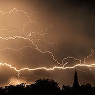 Bliksemschichten tijdens onweer over bomen en kerktoren